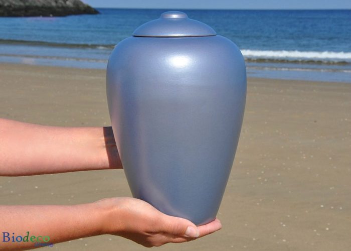 Biologisch afbreekbare zee-urn Classic Aqua in handen gedragen, op het strand van Scheveningen voor de zee