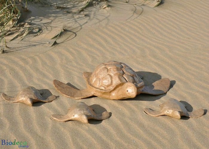 De zee-urn Schildpad op het strand van Scheveningen, handvervaardigd van gerecycled papier, omringd door drie mini Schildpad zee-urnen